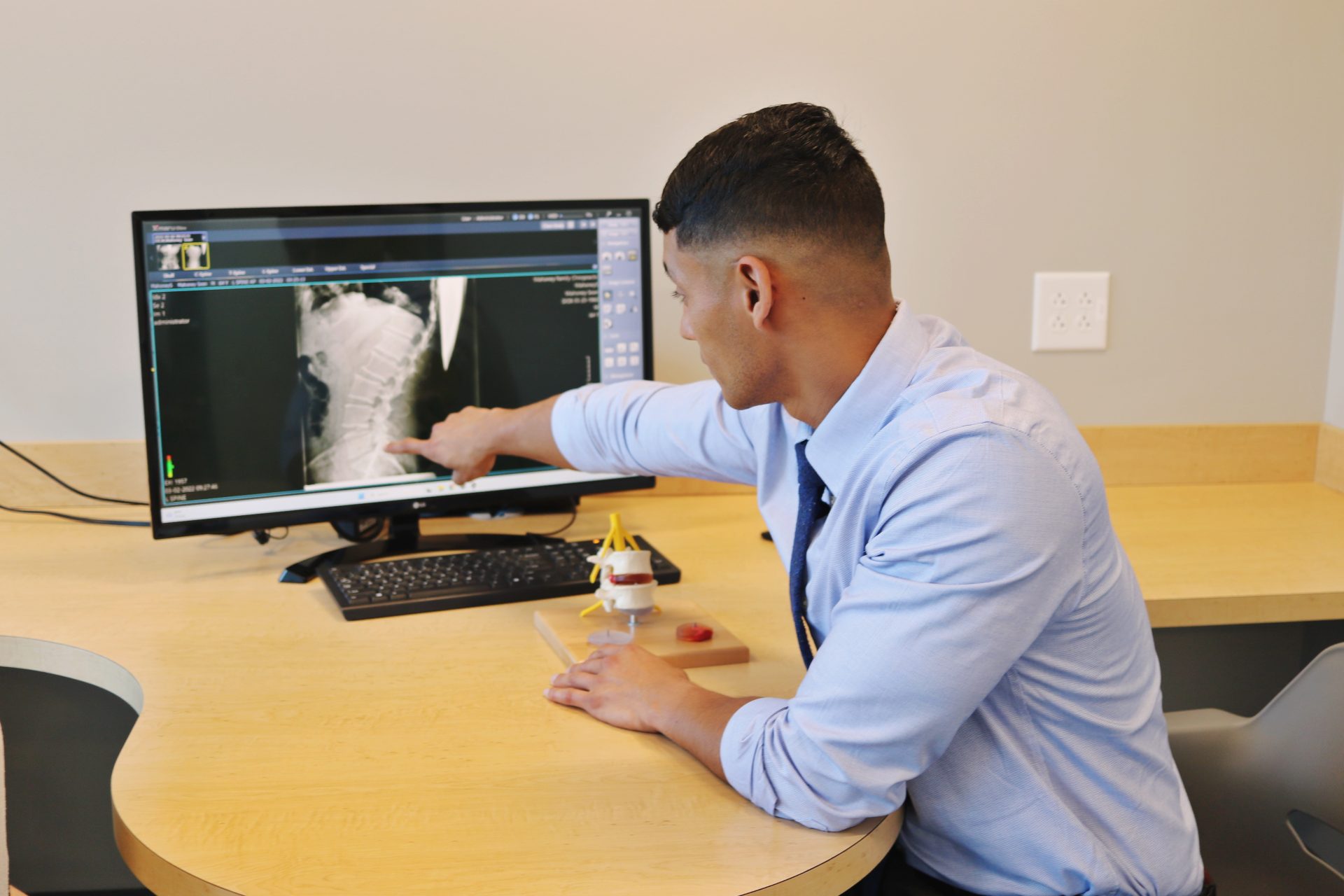 Chiropractor reviewing spinal X-ray and pointing out findings during patient consultation.