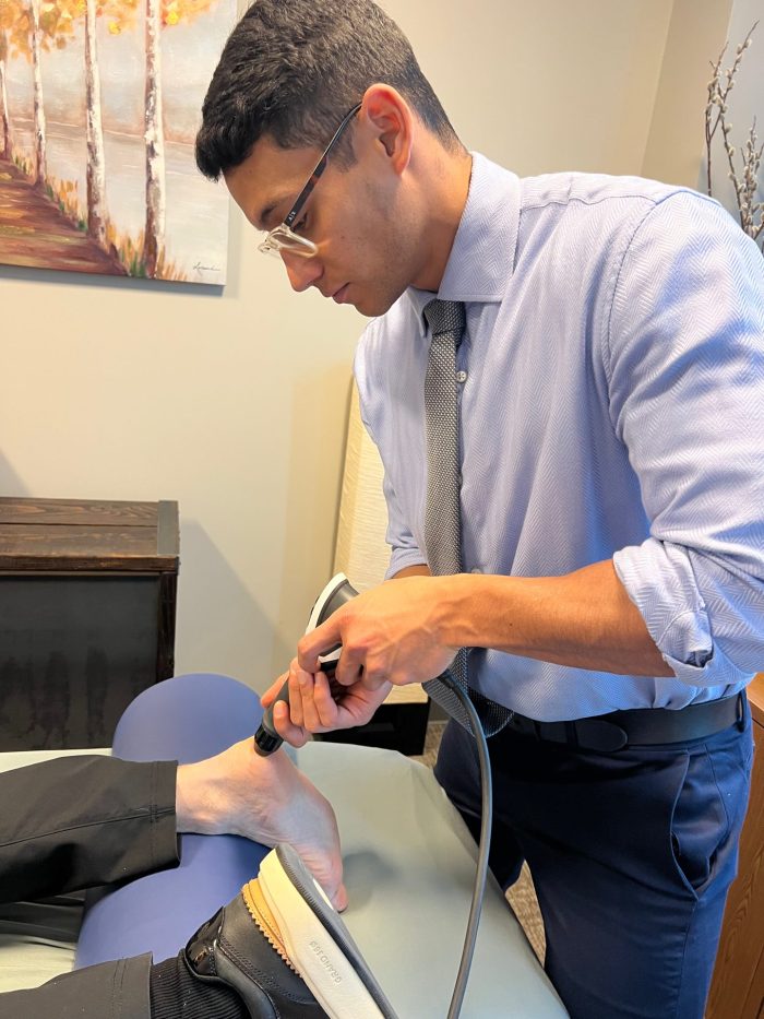 Clinician using a handheld therapy device on a patient’s ankle and foot.